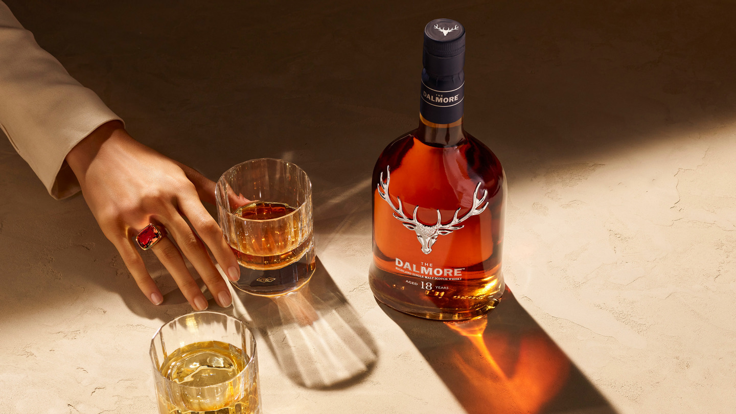 Hand with gem-studded ring reaches for a whisky glass